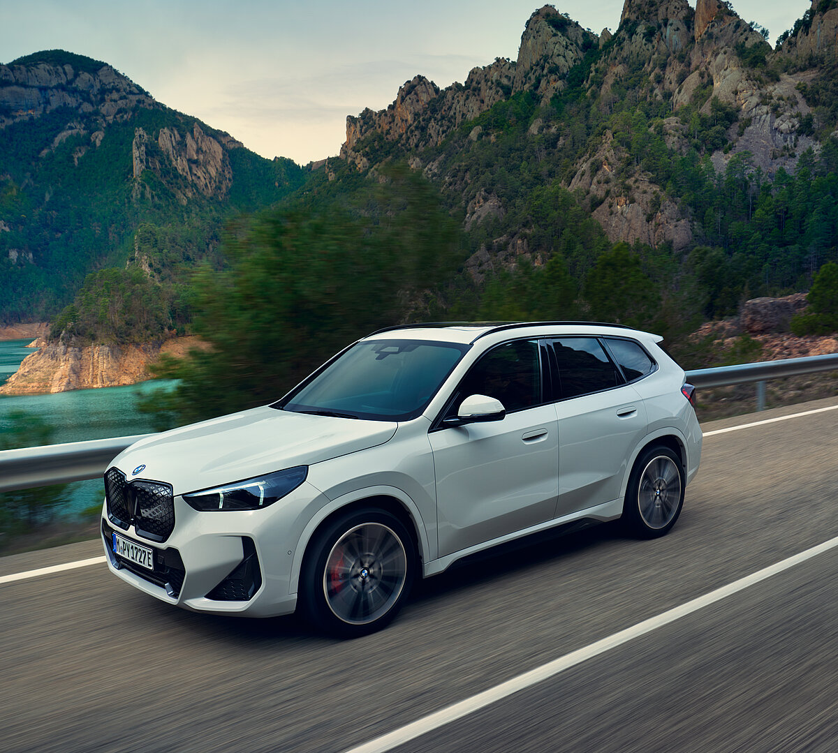 Weißer BMW SUV fährt auf Küstenstraße mit Bergblick