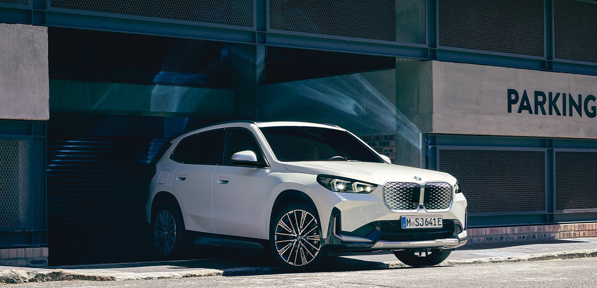 Ein weißer BMW iX fährt aus einem Parkhaus