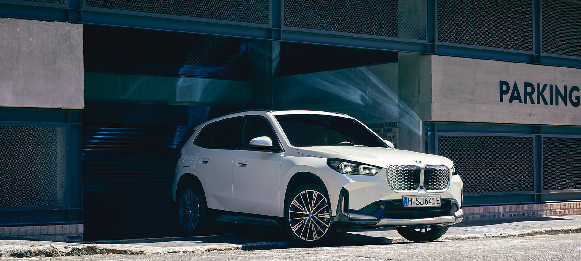 Ein weißer BMW iX fährt aus einem Parkhaus