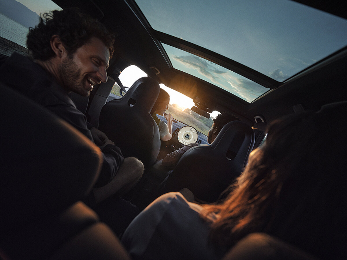 Zwei Personen sitzen lachend im Auto bei Sonnenuntergang.